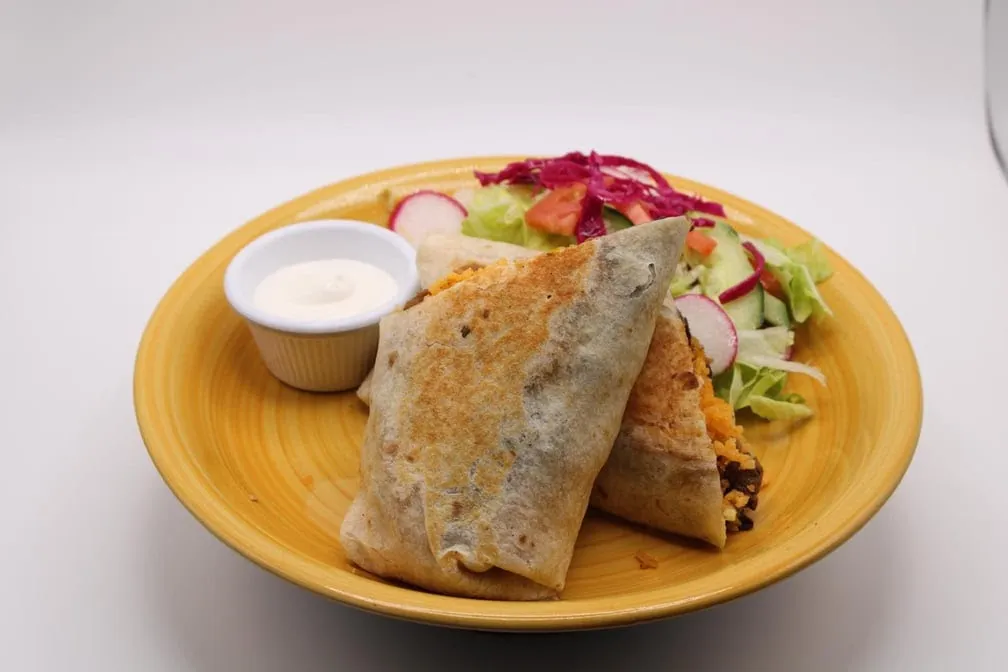 Grilled burrito cut in half on a yellow plate with a side salad and sour cream