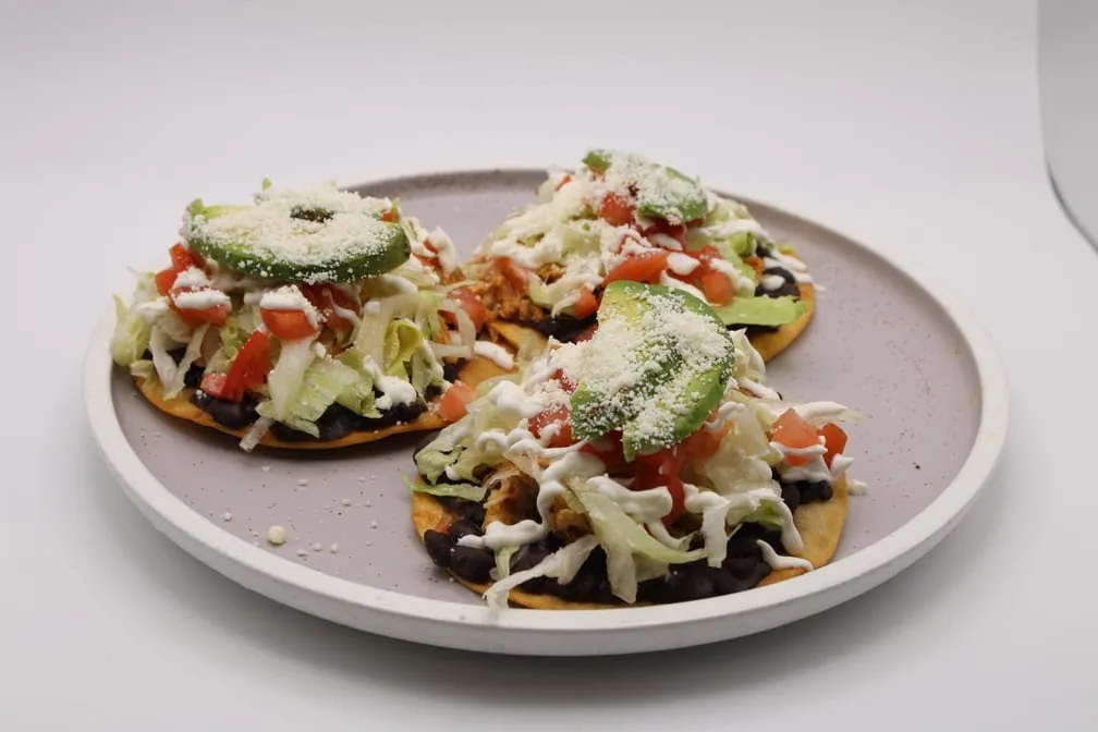 Three chicken tostadas with black beans, lettuce, tomato, avocado, crema and queso fresco