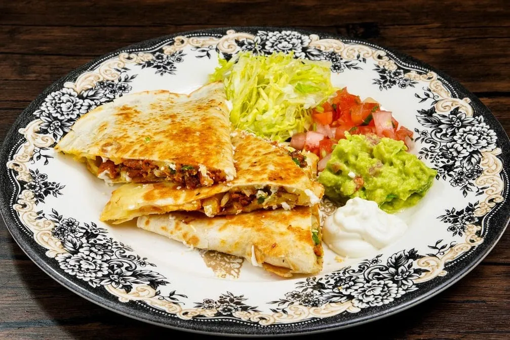 Flour tortilla quesadilla cut in wedges, with guacamole, pico de gallo, lettuce and sour cream