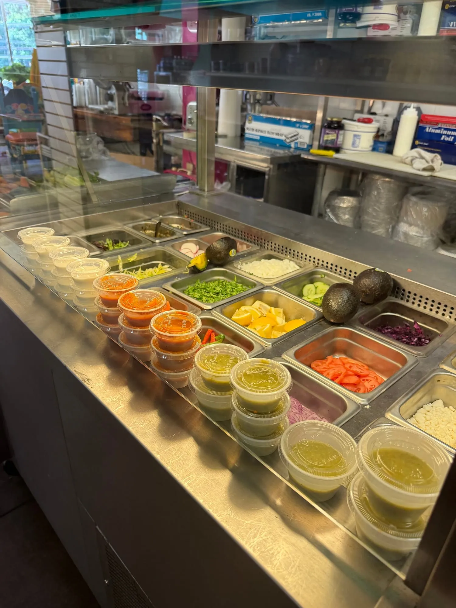 Toppings bar with cups of red and green salsa, avocados, lemons, cilantro, onion, tomato and red cabbage